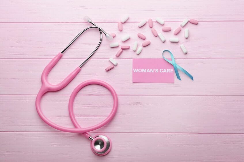 business card with text womans care, ribbon and stethoscope on pink wooden background